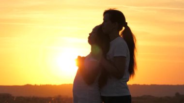 Anne kızına sarılır, onlar güzel gün batımını severler. Mutlu aile anne ve kızı gün batımında bir tarlada. Mutlu çocuk ve çocuk ailesi kavramı. Anne ve bebek parkta, tarlada, güneşte yürüyor.
