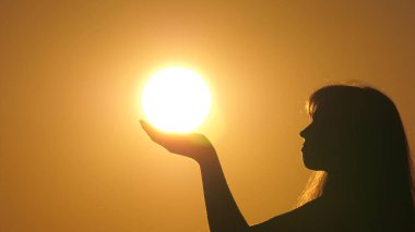 Mutlu kadın avuçlarında güneş tutuyor. Gün batımında dua eden bir kızın silueti. Seyahat ve macera konsepti. Güneşin ihtişamını takdir et. Din ve Tanrı 'ya inanç. Kızların elinde güneş ışığı.