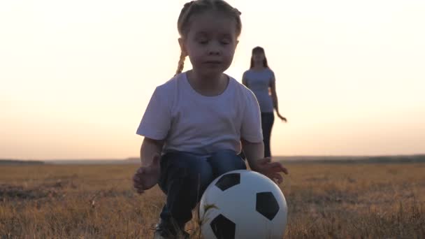 Glückliche Familie und Kind haben Spaß beim Fußballspielen im Park. Das Kind kickt Ball. Mutter und Tochter spielen Fußball auf dem Feld im Sonnenuntergang. Teamwork von Kind und Mutter. Gesunde Sportfamilie — Stockvideo