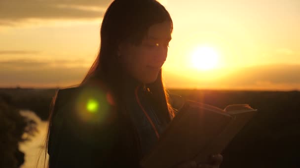 Une fille tient la Bible dans ses mains et étudie la parole de Dieu au lever du soleil sur le sommet de la montagne. Une femme lit un livre dans les rayons du soleil. L'homme lit la Bible à l'extérieur. Recherche de la vérité dans les Écritures. — Video