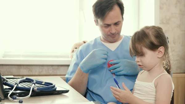 Un pediatra ve a un niño pequeño. El médico escucha al corazón de los niños con un estetoscopio. Clínicas privadas. Cuidado de pediatra masculino profesional que juega con un niño pequeño en la oficina — Foto de Stock