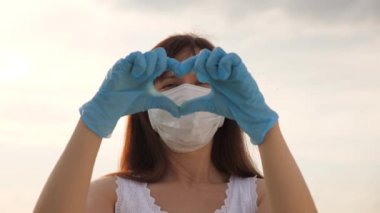Koruyucu maske ve tıbbi eldiven takmış yüzü olmayan bir kadın ellerinde bir kalp sembolü gösteriyor. Genç kadın doktorları sever. Salgın, covid 19. Kadın doktor kalp ve hastalara sevgi gösteriyor..