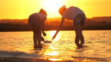 Çocuklar suya kağıttan bir tekne koydular. Kızlar kağıt teknelerle oynarlar. Childs bir tekneyi nehre fırlattı. Kağıt filosu. Mutlu aile fantezisi, çocukluk hayali, macera ve seyahat konsepti.