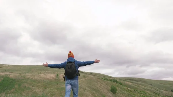 A free tourist, a happy traveler goes to mountains with open arms, catches wind with his hands. Man is traveling with a backpack enjoying beautiful landscape of hills. Travel and adventure concept