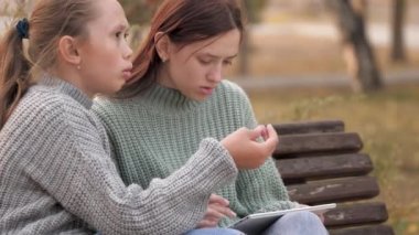 Modern dijital tabletle parkta bankta oturan kız öğrenciler. Üniversiteden, üniversiteden, okuldan, öğretmenlik derslerinden. Çevrimiçi eğitim ve çocuklar için bilgi. Gençlik yaşam tarzı, bilgisayar oyunları.