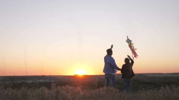 Het kind en vader hebben plezier met vliegeren in de lucht. Gelukkige familie. Papa speelt met zijn dochter samen en lanceert een vlieger in het park bij zonsondergang. Familie lanceert kleurrijke papieren vliegtuigen in de lucht — Stockvideo