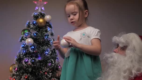 Criança e Papai Noel decorar a árvore de Natal. Uma menina e Papai Noel penduram lindas bolas na árvore. Férias e celebrações. Família crianças férias de inverno. Feliz Natal!. — Vídeo de Stock