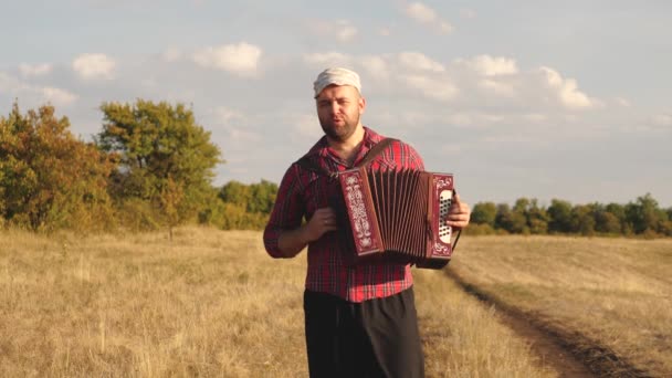 Människan spelar dragspel i solen. Konstnären uppträder utomhus, sjunger och spelar musikinstrument. Tradition och fest på landsbygden. Glada man är musiker, han sjunger och spelar musikinstrument — Stockvideo