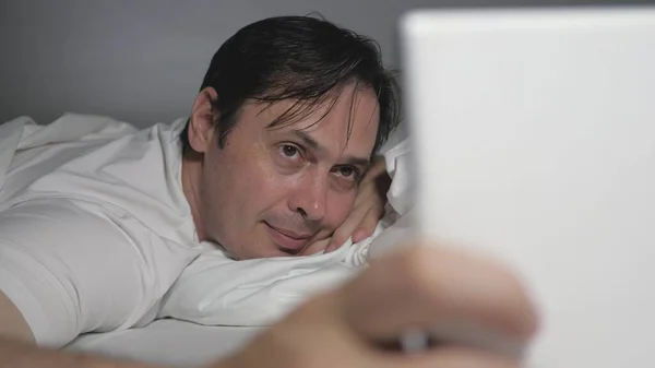 Ένας άντρας ξεκουράζεται στο σπίτι του το βράδυ πριν κοιμηθεί. Έλεγχος ταχυδρομείου, ανάγνωση ειδήσεων σε ένα σύγχρονο gadget. Ένας άντρας στο σπίτι ξαπλώνει στον καναπέ στο σαλόνι, χρησιμοποιώντας ένα tablet ενώ ψωνίζει σε ένα ηλεκτρονικό κατάστημα. — Φωτογραφία Αρχείου