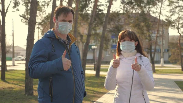 男も女も街中の防護マスクをはいている。人々はウイルスのための医療マスクをつけ、親指を立てる。コロナウイルスパンデミックの健康と安全の概念,コロナウイルス, COVID-19.ウイルス対策 — ストック写真