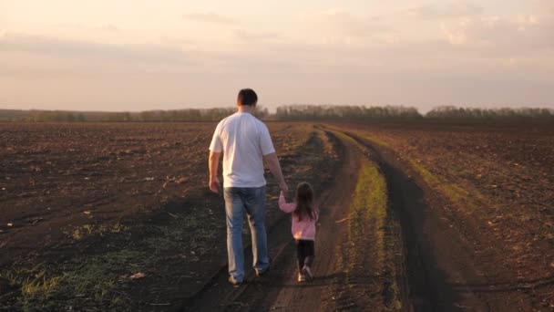 Uma família feliz, um pai agricultor e uma filha estão andando no campo arado. O miúdo dá a mão aos pais. O bebé e o pai estão a atravessar o campo. A criança e o pai estão andando em sua própria terra. — Vídeo de Stock