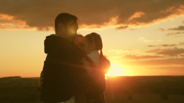 O pai abraça a filha e a mulher à noite no parque ao pôr-do-sol. Abraços familiares felizes ao sol. Um bebé saudável nos braços do papá. Criança feliz, mãe e pai estão brincando. família feliz e conceito de infância — Vídeo de Stock