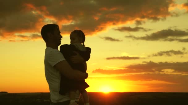Zdravé dítě si hraje s tátou. Táta objímá a přikrývá svou dcerku bundou za chladného večera v parku při západu slunce. Otec a šťastné dítě víří na poli na slunci. Šťastná rodina a dětství — Stock video