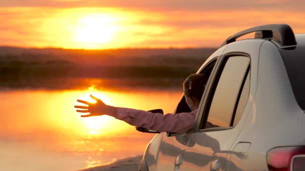 Eine freie Reisende wedelt mit den Armen aus ihrem Auto und genießt den Sonnenaufgang über dem See und die wunderschöne Landschaft. Die Fahrerin hielt mit dem Auto auf dem Campingplatz an und sah den Sonnenuntergang. — Stockvideo