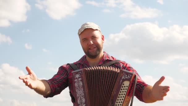 Man plays accordion in sun. Artist performs in open air, sings and plays musical instrument. Tradition and celebration in countryside. Cheerful man is musician, he sings and plays musical instrument — Stock Video