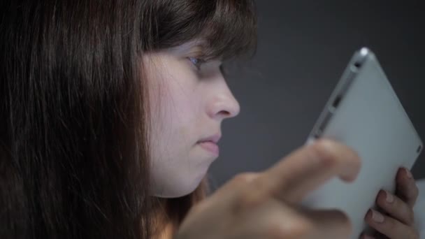 Una mujer en casa se encuentra en el sofá en la sala de estar, utilizando la tableta mientras va de compras en una tienda en línea. Mujer trabaja en línea en casa por la noche antes de ir a la cama. Comprobación de correo, leer noticias en gadget moderno — Vídeos de Stock