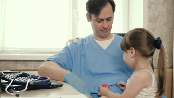 Ein kleines Kind wird von einem Kinderarzt untersucht. Der Arzt hört dem Kinderherz mit einem Stethoskop zu. Privatkliniken. Fürsorglicher männlicher Kinderarzt spielt mit einem kleinen Kind im Büro — Stockvideo