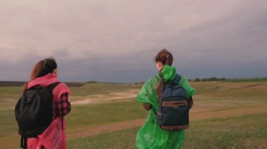 Özgür kadınlar tepenin kenarına yürürler, sevinirler, ellerini çırparlar ve mutlulukla el sallarlar. Turist kızlar sırt çantalarıyla renkli yağmurluklarla seyahat ederler. Takım çalışması gezginleri. Seyahat