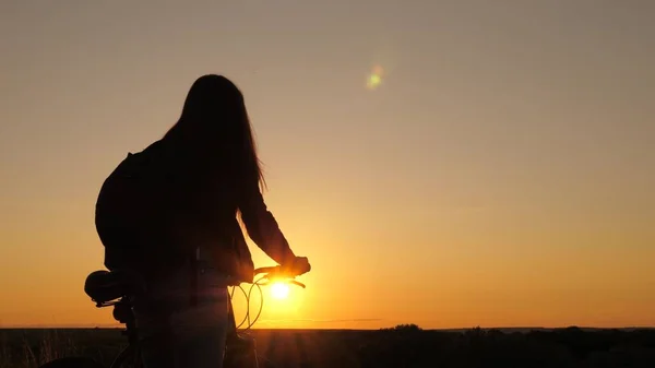 Giovane donna viaggia in bicicletta al tramonto. avventura e concetto di viaggio. Ragazza sana turista va in bicicletta ai margini della collina, godendo la natura e il sole. Bella ciclista donna sta riposando nel parco. — Foto Stock