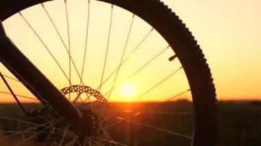 Bisiklet çarkı dönüyor. Bisiklet tekerleğinin tellerinin arasından güneş parlıyor. Bisiklet tekerleği dönüşü. Bisiklet eğitimi. Spor Sağlıklı Yaşam Tarzı. Bisikletçi direksiyona bakar.