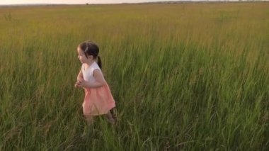 Mutlu küçük kız kollarını açmış yeşil bir tarlada koşuyor. Çocuk temiz havanın tadını çıkarıyor kahkahalar atıyor ve ellerini çırpıyor. Neşeli bir çocuk yeşil çimlerde koşar.