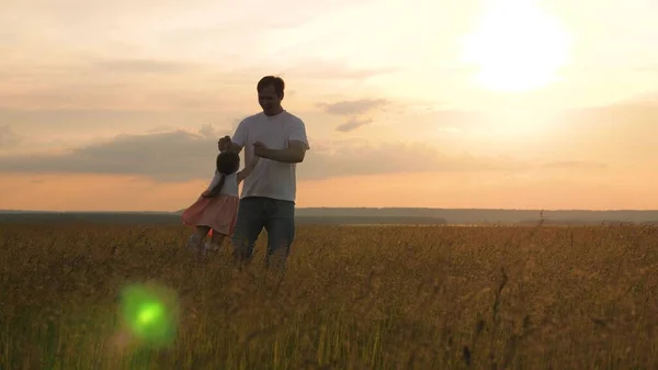 Szczęśliwa córeczka bawi się z tatusiem, tata okrąża dziecko po ramionach. Dziecko lubi latać. Zdrowe dziecko śmieje się podczas lotu. Ojciec i dziecko bawią się na polu na zielonej trawie. Dzień wolny od pracy. — Zdjęcie stockowe