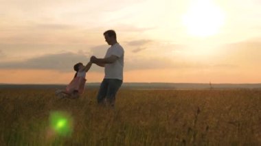 Mutlu küçük kız babasıyla oynuyor, baba da çocuğun etrafında kol kola dolaşıyor. Çocuk uçmayı seviyor. Sağlıklı bir çocuk uçarken güler. Baba ve çocuk yeşil çimlerin üzerinde bir tarlada oynuyorlar. Aile tatili.