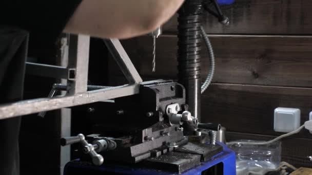 Un mecánico mide una parte en un taller. Una máquina perforadora perfora un agujero en una parte metálica. Un cerrajero en una fábrica en una tienda de cerrajería. Taladradora. El conductor perfora el agujero en la pieza de hierro — Vídeos de Stock