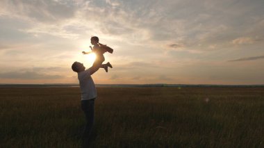 Babam mutlu kızını mavi gökyüzüne fırlattı. Baba ve küçük bir çocuk sahada birlikte oynuyorlar, gülüyorlar ve sarılıyorlar. Aile seyahati. Çocuk ebeveynin kollarında. Baba günü izinli. Mutlu aile ve çocukluk