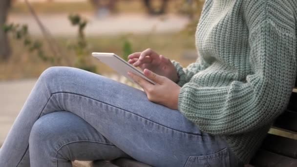 Ręce ucznia dotykają ekranu dotykowego tabletu w parku na ławce. Dziewczyna używająca tabletu cyfrowego drukuje wiadomości na ulicy. Kobieta pracująca z tabletem na zewnątrz — Wideo stockowe