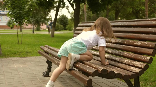 Een klein kind speelt in het park, klimt op de bank. Gelukkig meisje loopt op straat onder toezicht van ouders. Hij staat op een bankje in het park. Gelukkige familie en jeugd concept. Gezonde baby buiten — Stockfoto