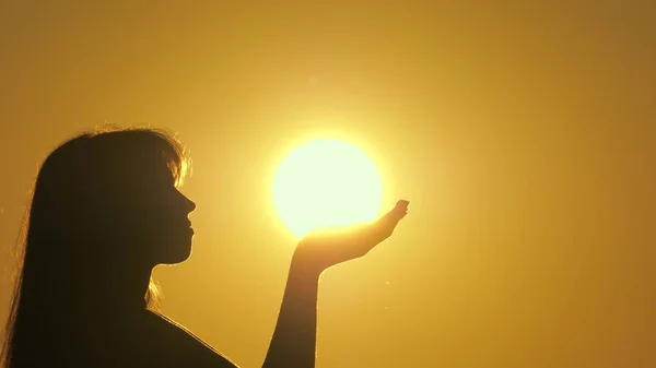 Silhouette of a girl praying in rays of sunset. Sunlight in girls hands. Happy woman holds sun on her palms. Travel and adventure concept. Admire glory of sun. Religion and belief in God. — Stock Photo, Image