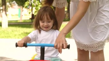 Annesi küçük kızına bisiklet sürmeyi öğretiyor. Mutlu bir aile ve sağlıklı bir çocukluk. Anne çocuğuyla dışarıda oynuyor. Çocuk bisiklet sürmeyi öğreniyor. Ebeveyn ve küçük kız parkta yürüyor..