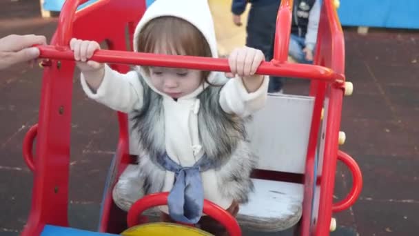 A criança brinca no parque infantil e balança no carro de brinquedo. A menina está rindo e se divertindo, balançando no balanço, brincando no playground com sua mãe. Família feliz e infância, emoções positivas — Vídeo de Stock