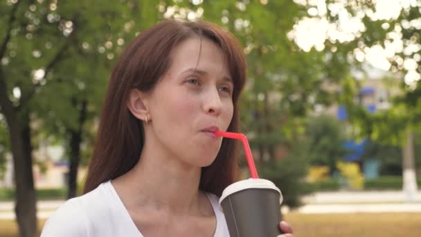 Genç ve güzel bir iş kadını, şehir parkında bir fincan lezzetli kahve eşliğinde gülümsüyor. Mutlu kız dışarıda sıcak aromatik çay içiyor.. — Stok video