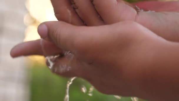 男は近くの通りで水で手を洗っている。手のひらの下からきれいな水のスプラッシュ、あなたの手を洗う。衛生的で清潔感のある健康コンセプト。健康な子供だ。通りを洗うために. — ストック動画