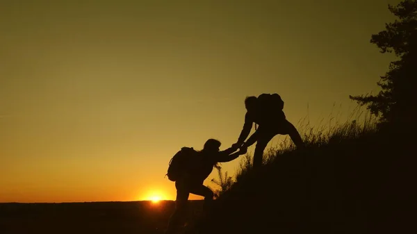 ハイカーのグループのチームワークのシルエットは、山、丘を登るのに役立ちます。ユーリスティー日没時に山に登ると、手を握って。観光客のチームワーク、トップに登ると友人と握手. — ストック写真