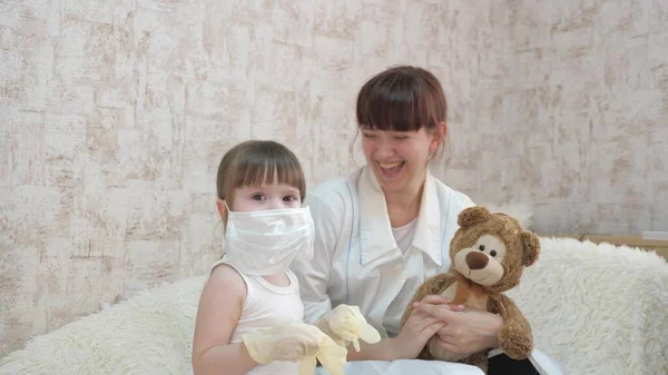 Kind en zijn moeder spelen doktertje, dragen medische handschoenen en een beschermend masker. Meisje speelt met medisch masker. Kind speelt in het ziekenhuis. Game doet zich voor als dokter, verpleegster.. — Stockfoto