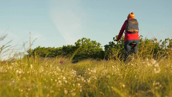 Caminhante mulher jovem monta uma bicicleta no campo e grama apreciando a natureza e ar fresco. Menina livre viaja com bicicleta na natureza. Conceito de viagem. O ciclista treina ao ar livre. Um estilo de vida desagradável. Pedalar, fitness — Fotografia de Stock