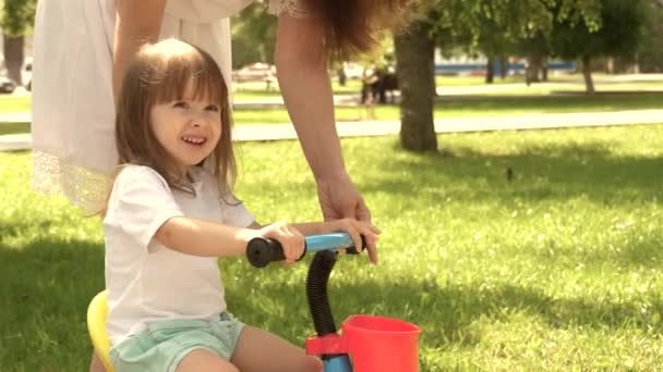 子供は自転車に乗ることを学ぶ。母は娘に自転車に乗るように教えている。幸せな家族と健康な子供時代。母は屋外で子供と遊んでいる。親と娘が公園を歩く. — ストック動画