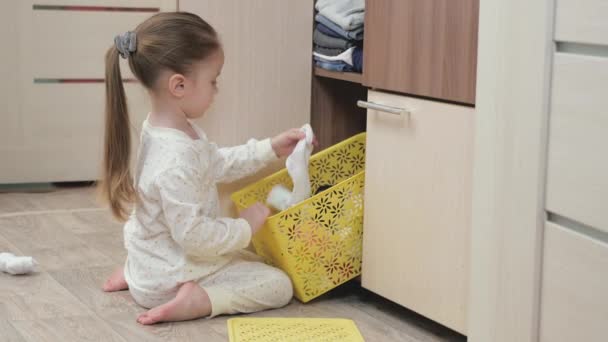 Un niño en pijama abre un armario y busca su ropa. La niña juega en la habitación de los niños. El chico juega y tira sus cosas de la caja. Hija juega con la ropa en casa — Vídeos de Stock