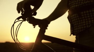 Bisikletçi güneşin altında bisiklet gidonunu tutuyor ve parkta dinleniyor. Bisikletin yanındaki tepede duran bir turist doğanın ve güneşin tadını çıkarıyor. Gezgin gün batımında bisikletle seyahat eder. Macera konsepti
