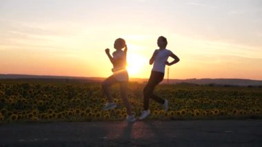 Spor kızlarını ısıtın. Akşam koşusu antrenmanı. Spor gençleri gün batımının parıltısıyla yol boyunca koşar. Sağlıklı koşu ve açık hava egzersiz konsepti. Kızlar koşuyor. Özgürlük, hareket halindeki hayat, sağlık.