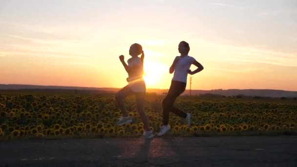 Spor kızlarını ısıtın. Akşam koşusu antrenmanı. Spor gençleri gün batımının parıltısıyla yol boyunca koşar. Sağlıklı koşu ve açık hava egzersiz konsepti. Kızlar koşuyor. Özgürlük, hareket halindeki hayat, sağlık. — Stok video
