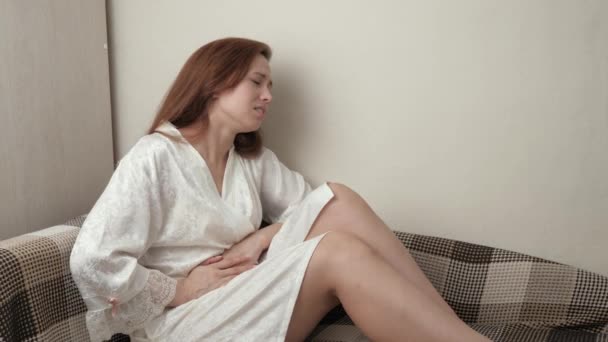 Ung kvinna som ligger på soffan och kramar magen och lider av buksmärta. Attack av blindtarmsinflammation. Sjuk flicka upplever mensvärk, vilar på soffan. Gastrit, menstruationssmärta. Bukspottkörteln gör ont — Stockvideo