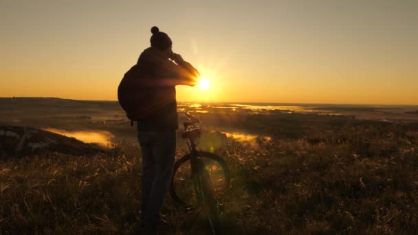 Mladý cestovatel stojí na kraji hory, pije čaj a těší se při východu slunce z přírody. Volný turista cestuje s kole v přírodě a pije čaj na slunci. Cyklista odpočívá. Sportovní životní styl. — Stock video