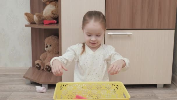 Ein Kind im Schlafanzug öffnet einen Schrank und sucht nach seiner Kleidung. Kleines Mädchen spielt im Kinderzimmer. Das Kind spielt herum und wirft seine Sachen aus der Box. Tochter spielt mit Kleidung zu Hause — Stockvideo