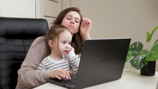 Moeder werkt met een laptop en speelt met haar dochtertje. Mam werkt en voedt kinderen op. Zakenvrouw in functie met een kind. Werken aan een computer als freelancer thuis op afstand. — Stockvideo