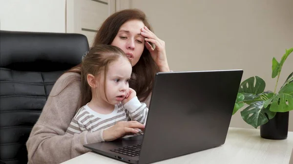 妈妈和笔记本电脑一起工作，和她的小女儿一起玩。妈妈在工作和抚养孩子一个带着孩子的女商人在家远程做计算机自由职业者的工作. — 图库照片