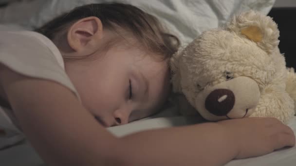 Çocuk, çocuk odasındaki kanepede uyur. Uyuyan bebek mutlu ve kaygısızdır. Oyuncak ayıya sarılır. Anne çocuğunu bir battaniyeyle örttü. Rüyadaki mutluluk.. — Stok video